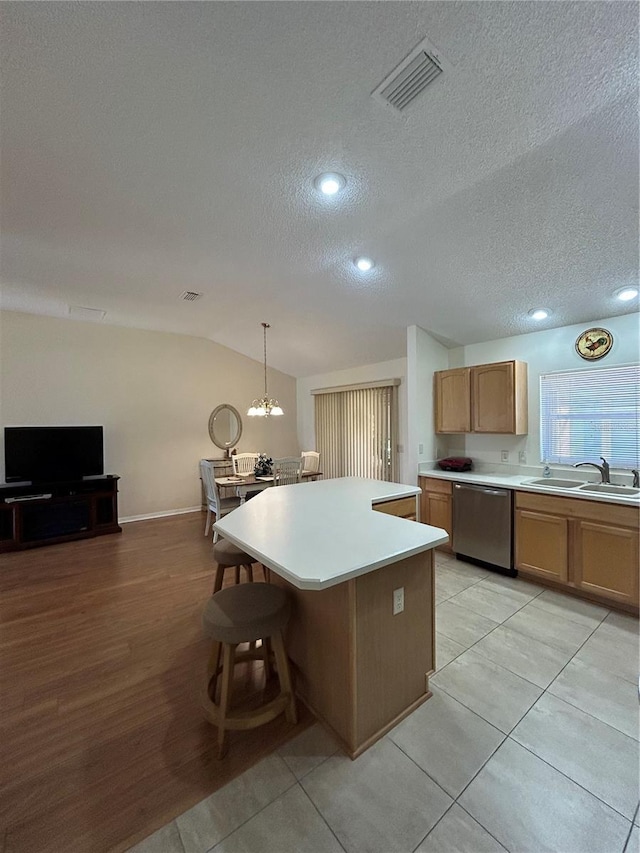 kitchen featuring visible vents, a center island, vaulted ceiling, stainless steel dishwasher, and a sink