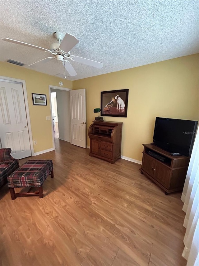 living area with ceiling fan, wood finished floors, baseboards, and a textured ceiling