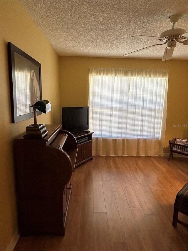 living area with plenty of natural light, a textured ceiling, wood finished floors, and a ceiling fan