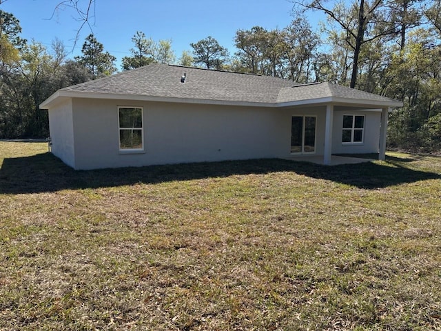 rear view of property featuring a yard, roof with shingles, and stucco siding