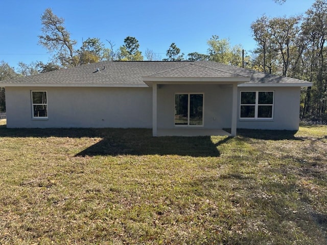 back of house with stucco siding, a shingled roof, and a yard