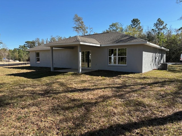 back of house with cooling unit, a lawn, a shingled roof, and stucco siding