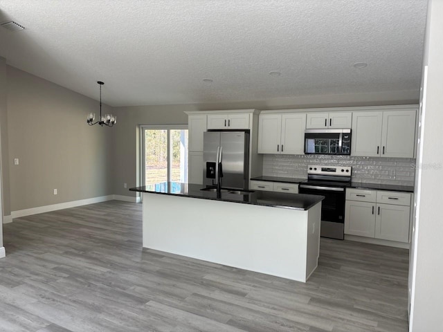 kitchen with dark countertops, backsplash, appliances with stainless steel finishes, and light wood-type flooring