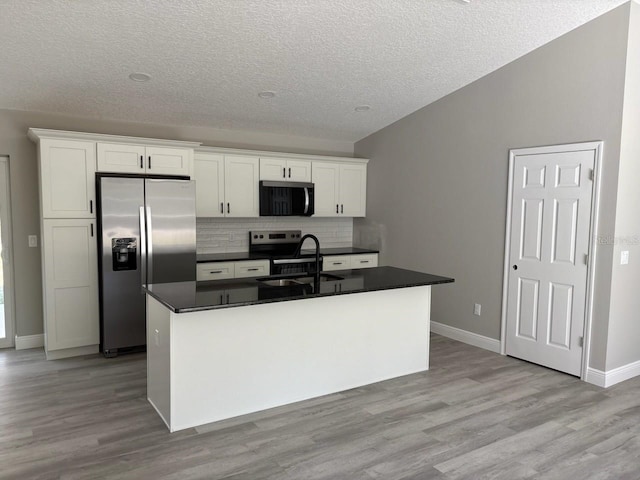 kitchen featuring light wood finished floors, a sink, white cabinets, dark countertops, and stainless steel fridge