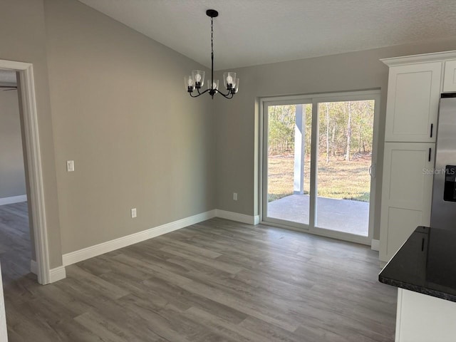 unfurnished dining area with baseboards, lofted ceiling, an inviting chandelier, and wood finished floors