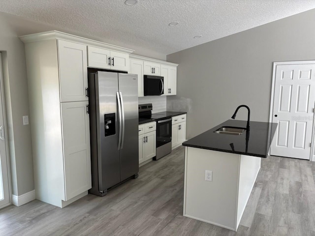 kitchen featuring dark countertops, light wood-type flooring, appliances with stainless steel finishes, white cabinets, and a sink