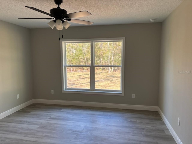 unfurnished room featuring a ceiling fan, wood finished floors, baseboards, and a textured ceiling