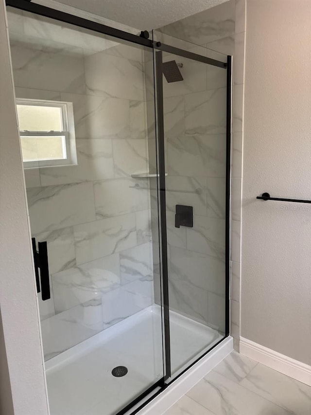 bathroom with marble finish floor, a stall shower, baseboards, and a textured wall