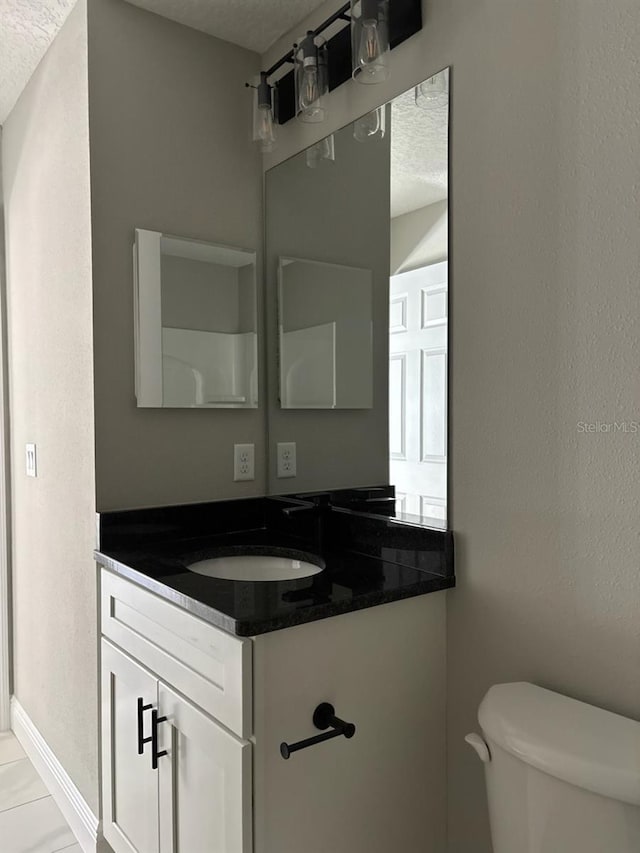 half bathroom with vanity, toilet, baseboards, and a textured ceiling