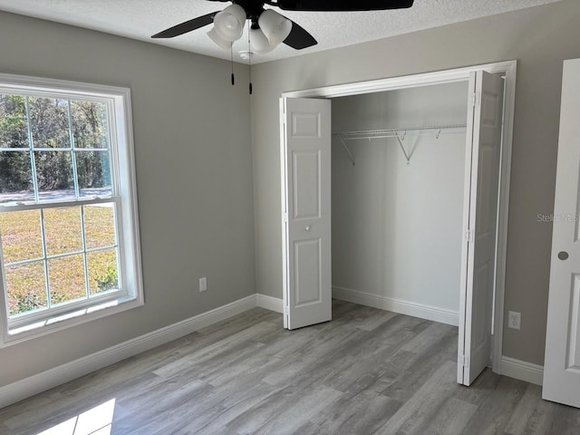 unfurnished bedroom with light wood-type flooring, baseboards, a textured ceiling, and a closet