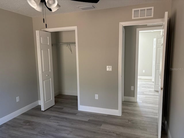 unfurnished bedroom featuring visible vents, baseboards, wood finished floors, a closet, and a textured ceiling