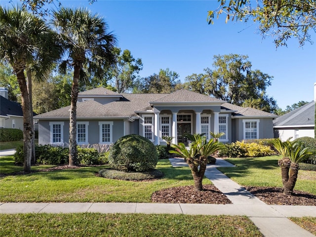 view of front facade with stucco siding, a front yard, and a shingled roof