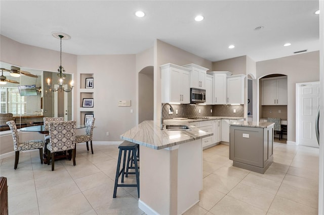 kitchen with light stone counters, arched walkways, a sink, decorative backsplash, and stainless steel microwave