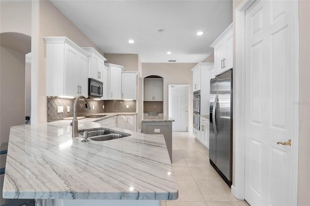 kitchen featuring tasteful backsplash, light stone countertops, a peninsula, light tile patterned flooring, and stainless steel appliances