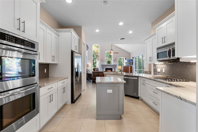 kitchen with a ceiling fan, a sink, appliances with stainless steel finishes, light tile patterned floors, and vaulted ceiling