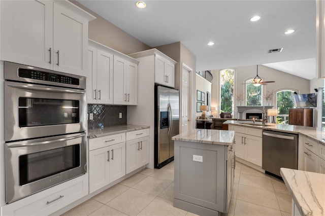 kitchen featuring a ceiling fan, a sink, tasteful backsplash, a lit fireplace, and appliances with stainless steel finishes