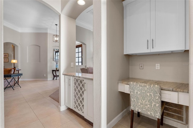 interior space featuring light tile patterned floors, baseboards, arched walkways, and ornamental molding