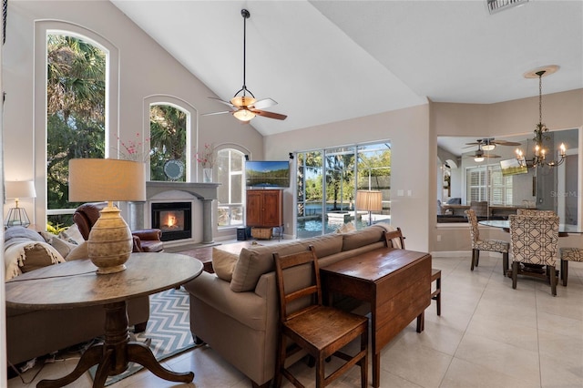 living area with light tile patterned floors, a glass covered fireplace, ceiling fan with notable chandelier, and high vaulted ceiling