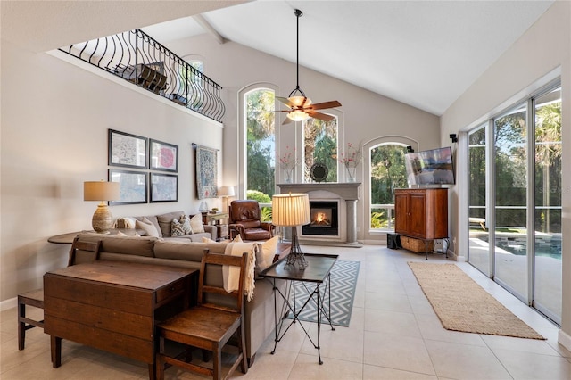 living room with baseboards, ceiling fan, light tile patterned floors, a glass covered fireplace, and high vaulted ceiling