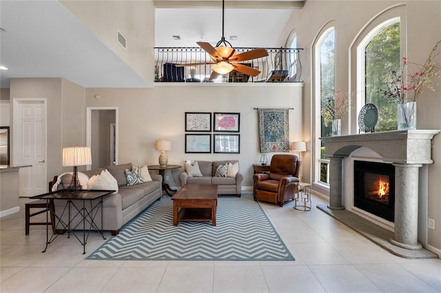 tiled living room featuring visible vents, baseboards, ceiling fan, a high ceiling, and a glass covered fireplace