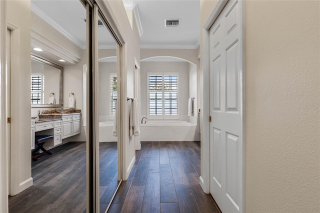 corridor featuring dark wood-style floors, visible vents, arched walkways, crown molding, and a textured wall