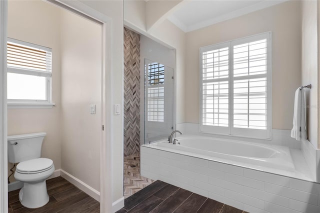 bathroom with a garden tub, toilet, wood finished floors, tiled shower, and baseboards