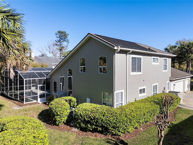 view of side of property featuring glass enclosure, driveway, and stucco siding