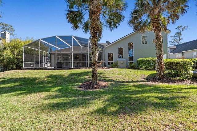 back of property featuring glass enclosure, a yard, and stucco siding