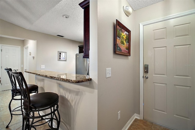 bar featuring visible vents, a textured ceiling, freestanding refrigerator, light tile patterned floors, and baseboards
