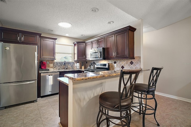 kitchen with dark brown cabinets, dark stone counters, a kitchen bar, appliances with stainless steel finishes, and a peninsula