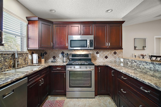 kitchen featuring dark brown cabinets, light stone counters, decorative backsplash, stainless steel appliances, and a sink