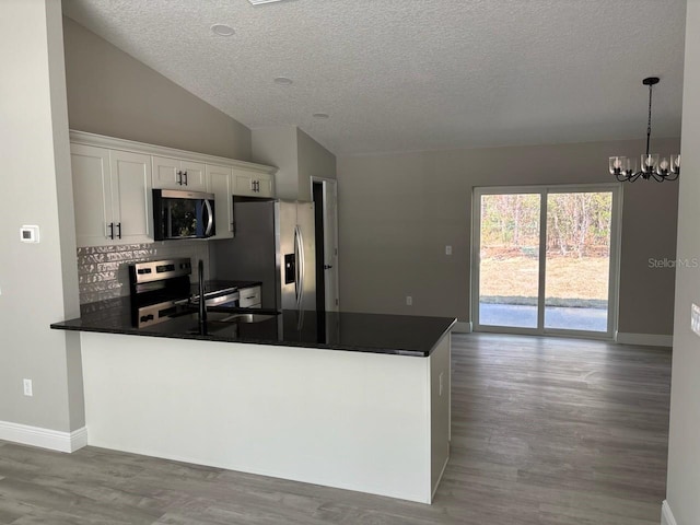 kitchen with dark countertops, wood finished floors, stainless steel appliances, a peninsula, and lofted ceiling