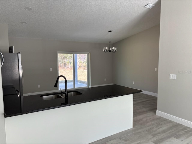 kitchen featuring visible vents, light wood finished floors, freestanding refrigerator, a sink, and dark countertops