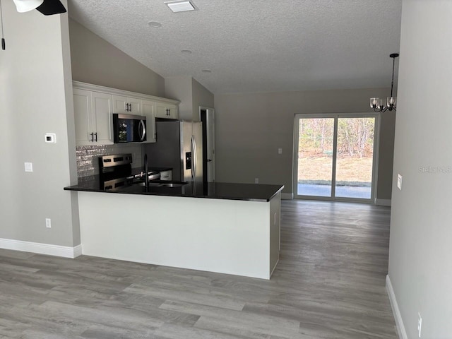 kitchen with lofted ceiling, dark countertops, appliances with stainless steel finishes, and white cabinets