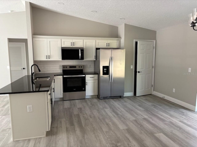 kitchen with a sink, vaulted ceiling, dark countertops, and stainless steel appliances