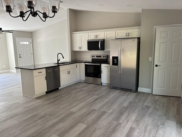 kitchen with lofted ceiling, a peninsula, a sink, appliances with stainless steel finishes, and dark countertops