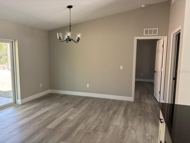 unfurnished room featuring wood finished floors, visible vents, a chandelier, and baseboards