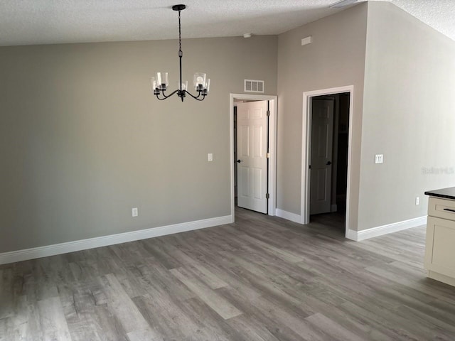 empty room featuring visible vents, light wood-style flooring, a textured ceiling, baseboards, and vaulted ceiling