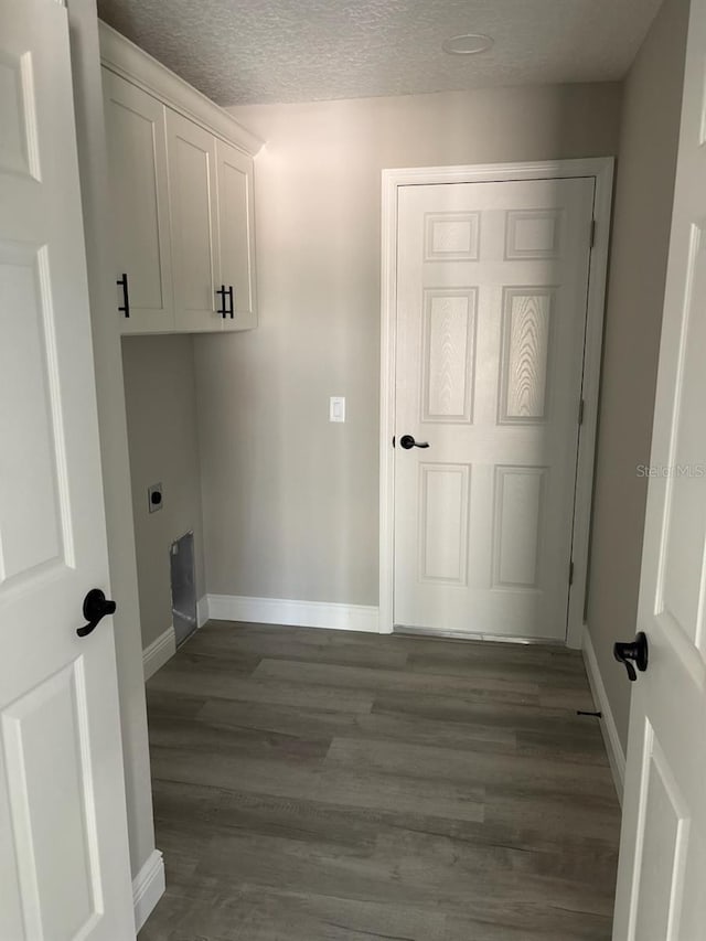 clothes washing area with baseboards, cabinet space, a textured ceiling, and dark wood-style floors