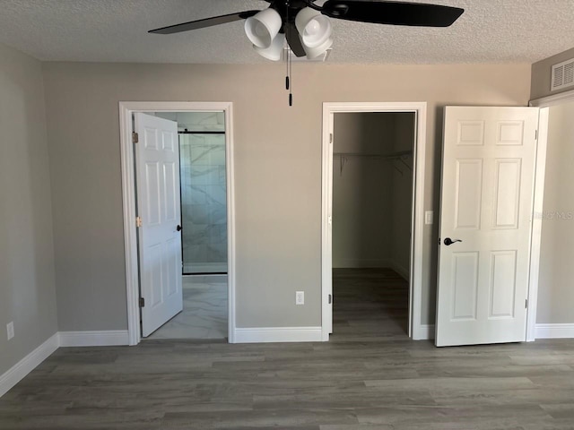 unfurnished bedroom with a textured ceiling, wood finished floors, a closet, baseboards, and a spacious closet