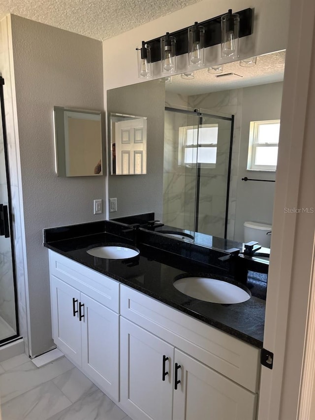 full bath with marble finish floor, a stall shower, a sink, a textured ceiling, and double vanity