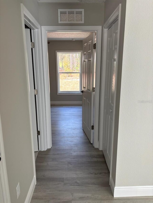 hallway with wood finished floors, baseboards, and visible vents