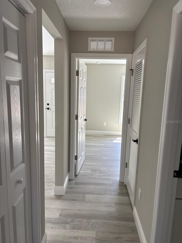 hall featuring light wood-style floors, visible vents, baseboards, and a textured ceiling