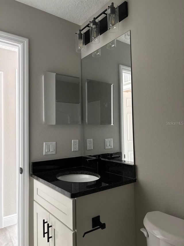 half bath featuring a textured ceiling, vanity, and toilet