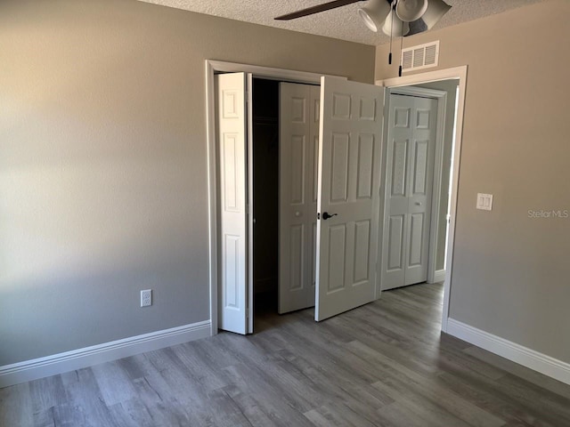 unfurnished bedroom with visible vents, a textured ceiling, wood finished floors, a closet, and baseboards