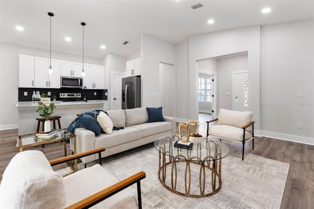 living area with recessed lighting, wood finished floors, visible vents, and baseboards