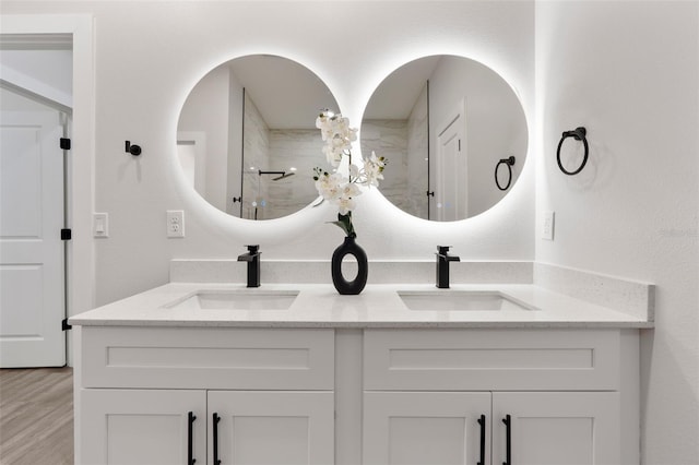 bathroom with double vanity, a shower with shower door, wood finished floors, and a sink