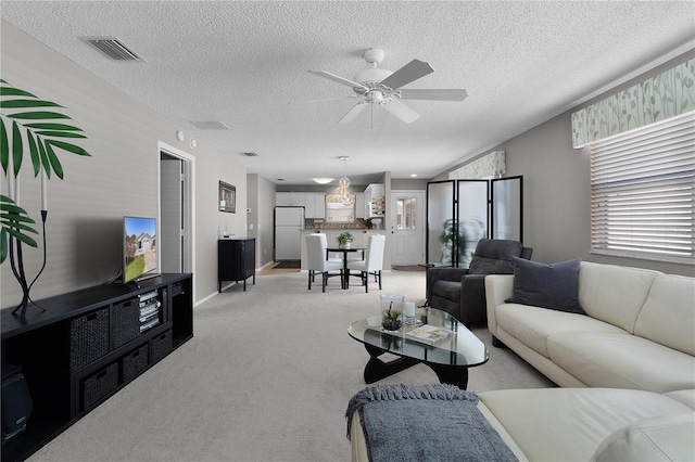 living area with visible vents, light colored carpet, a ceiling fan, and a textured ceiling