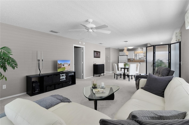 living room featuring light colored carpet, a textured ceiling, wallpapered walls, and a ceiling fan