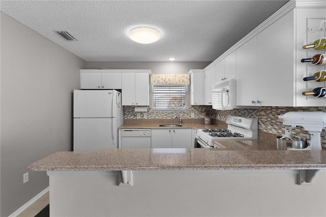 kitchen with visible vents, white appliances, tasteful backsplash, and a peninsula